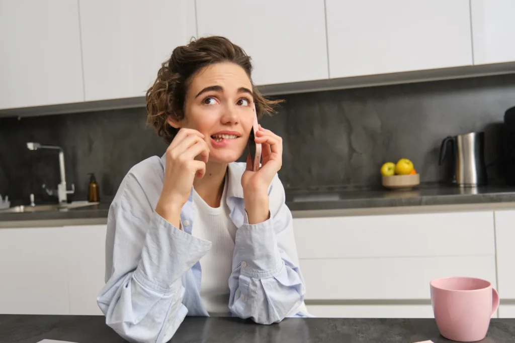 Mujer dudando mientras atiende una llamada comercial en la cocina